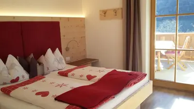 a bedroom with a bed with red sheets and a window at Singerhof in Castelrotto