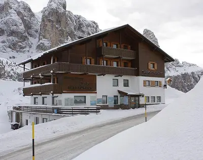 a large building in the snow in front of a mountain at Alpin Hotel & Restaurant Frara in Selva di Val Gardena