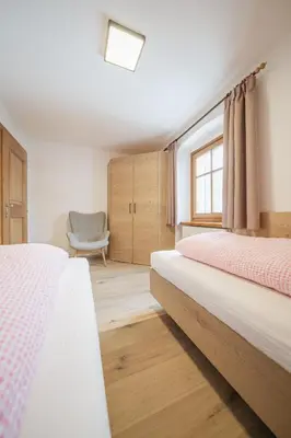 a bedroom with two beds and a chair at Apartments Carmen in Ortisei