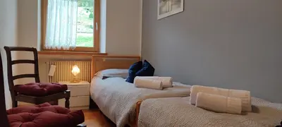 a bedroom with two beds and a chair and a window at Ai Grisi in Cavalese