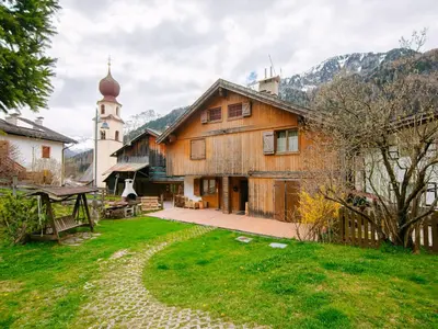a building with a clock tower and a green yard at Apartment Appartamento Crepaz by Interhome in Canazei