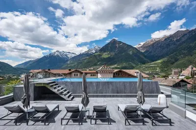 a patio with lounge chairs and a view of mountains at Hotel Sunnwies in Schenna