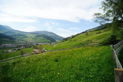 a green hillside with a town in the distance at Botenhof - Urlaub auf dem Bauernhof - Agriturismo in Sarntal