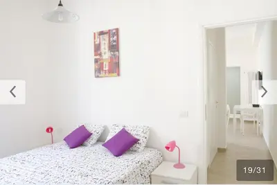 a white bedroom with a bed with purple pillows at Appartamento Bolzano Centro Talvera in Bolzano