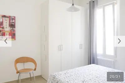 a white bedroom with a bed and a chair at Appartamento Bolzano Centro Talvera in Bolzano