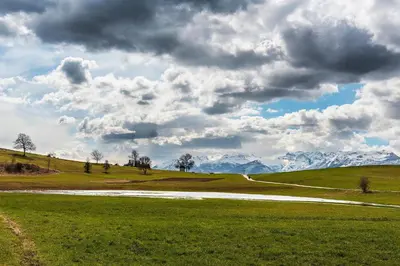 a field with a road and mountains in the background at APPARTAMENTO ROEN in Cavareno