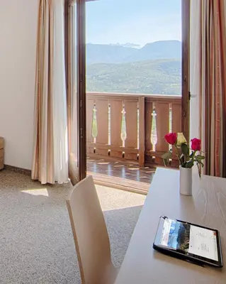 a room with a table with a tablet on it and a balcony at Pension Christl in Caldaro
