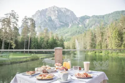 a table with plates of food on it next to a lake at Hotel Lago della Creta in San Vigilio Di Marebbe