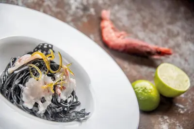 a white bowl of food with seafood and a lime at Hotel Lago della Creta in San Vigilio Di Marebbe