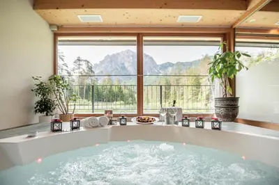 a bath tub in a room with a large window at Hotel Lago della Creta in San Vigilio Di Marebbe