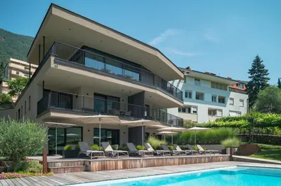 aominium building with a swimming pool and chairs and a building at Erbacher Living Nature Apartments Suites in Bolzano