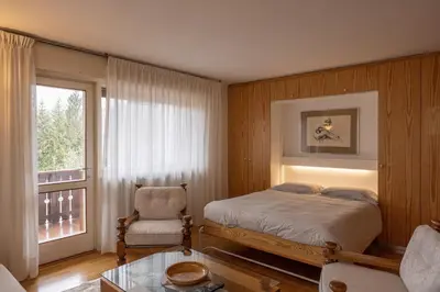 a bedroom with a bed and a chair and a window at Sorapis Mini - Monolocale Panoramico in Cortina dʼAmpezzo