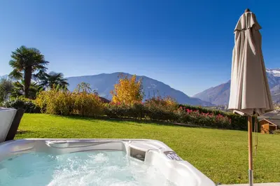 a hot tub in a field with an umbrella at Hotel Garni Katnau in Schenna