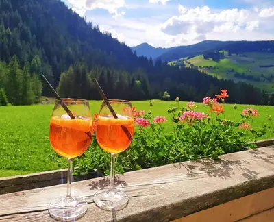 two wine glasses sitting on a wooden table with a field of flowers at romy's B&B in Braies