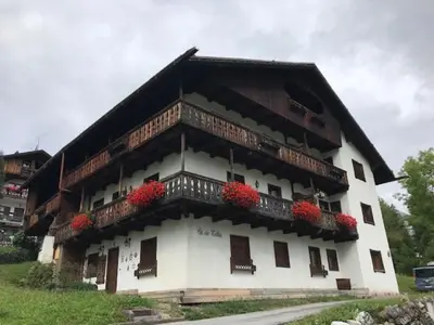 a building with red flowers on the balcony of it at Appartamento Crignes in Cortina dʼAmpezzo