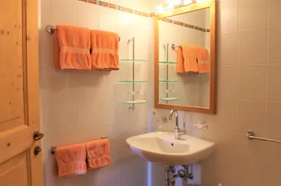 a bathroom with a sink and a mirror and orange towels at Hotel Landgasthof Lärchenwald in Collepietra