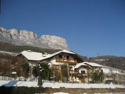 a house covered in snow with mountains in the background at Gfillhof Ferienwohnung 1 in Appiano sulla Strada del Vino