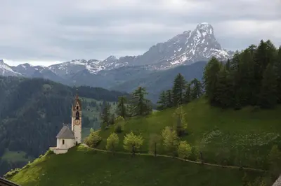 a church on top of a green hill with a mountain at Agriturismo Tolpei in La Valle