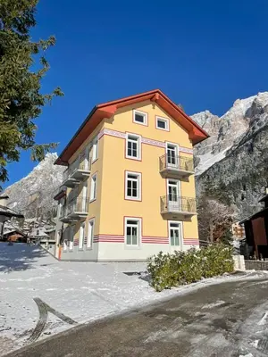 a yellow building with a red roof in the mountains at Appartamento Vale e Schena Cortina D'Ampezzo in San Vito di Cadore
