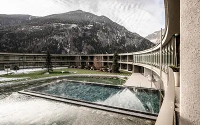 a building with a swimming pool and a mountain at OLM Nature Escape - Eco Aparthotel in Campo Tures