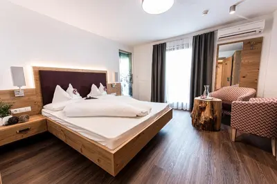 a bedroom with a large bed and a room with a chair at Alpenhof Lodge in Saltusio
