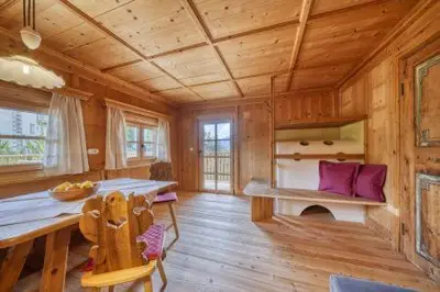 a wooden cabin with a dining table and purple pillows at Lothof in Schenna