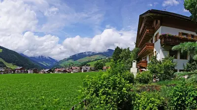 a building in a green field with mountains in the background at Pension Arnica B&B in San Vigilio Di Marebbe
