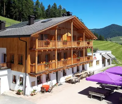 a large wooden building with a balcony and tables and umbrellas at Agriturismo Soleseid in San Vigilio Di Marebbe