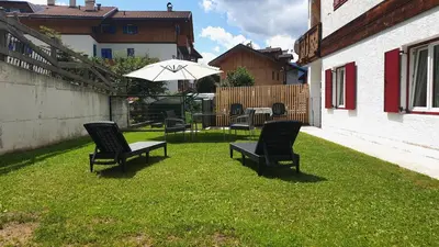a patio with chairs and an umbrella on the grass at Casa Il Giardino in Pozza di Fassa