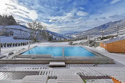 a swimming pool covered in snow with mountains in the background at Hotel Torgglerhof in Bressanone