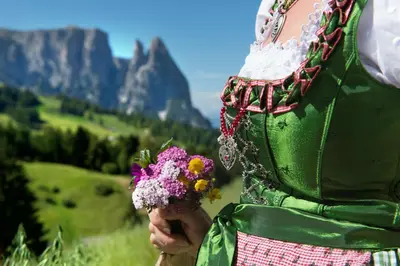 a woman holding a bunch of flowers with mountains in the background at Hotel Chalet Dolomites in Alpe di Siusi