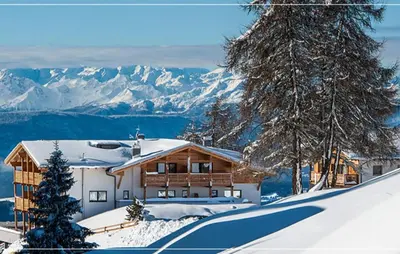 a house in the snow with mountains in the background at Hotel Chalet Dolomites in Alpe di Siusi