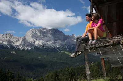 a man and woman sitting on the edge of a building with mountains at Condominio al Lago in Alleghe