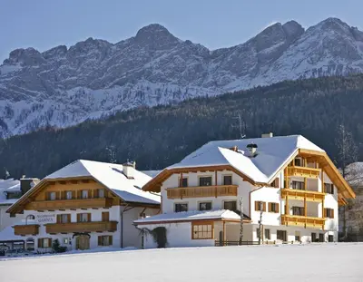 a building with snow covered roofs with mountains in the background at Appartements Steiner in Valdaora