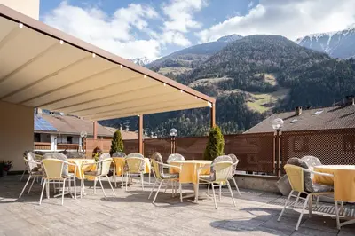a patio with tables and chairs with mountains in the background at Aparthotel Zum Schlössl in Villa Ottone