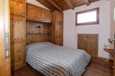 a bedroom with a bed with wooden cabinets and a window at Estate in montagna in San Vito di Cadore