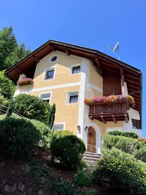 a yellow house with a balcony with flowers on it at Apartments Mauriz in Selva di Val Gardena