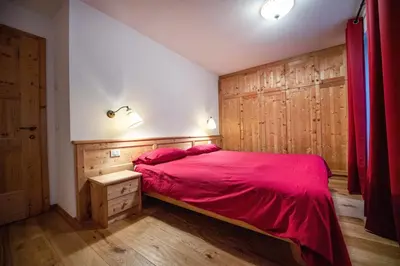 a bedroom with a red bed with a wooden wall at Cristina Hospitality in Ortisei