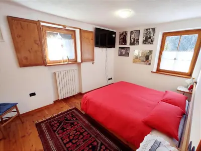a bedroom with a red bed and two windows at Casa Amabile in San Vito di Cadore