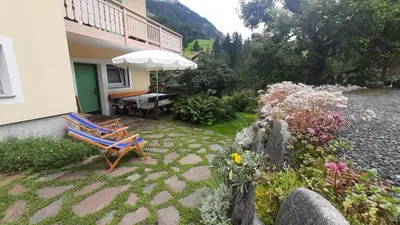 a patio with two chairs and an umbrella and flowers at Appartamento Zanoner Lorenzo in Moena