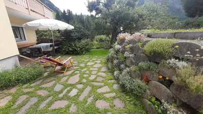 a garden with chairs and an umbrella and a stone wall at Appartamento Zanoner Lorenzo in Moena