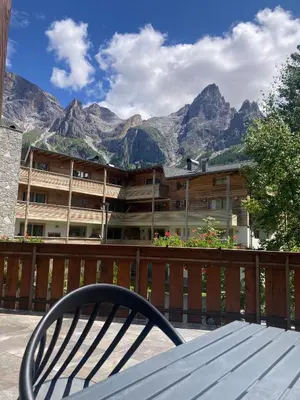 a chair sitting in front of a building with mountains at Appartamento con terrazza vista Pale di San Martino in San Martino di Castrozza