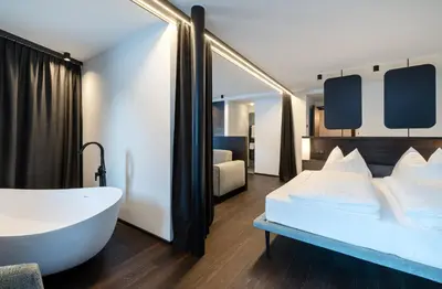 a bathroom with a tub and a bedroom with a bed at Hotel Mühlenerhof in Campo Tures