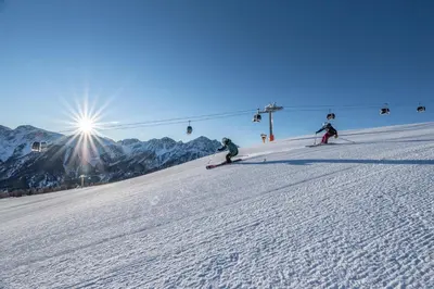 three people skiing down a snow covered slope with a ski lift at App Mittermairhof in Riscone