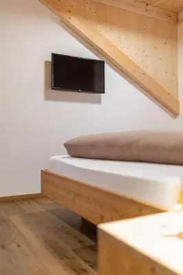a room with a bed and a tv on a wall at App Mittermairhof in Riscone