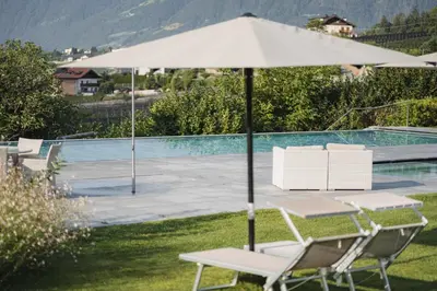 a table and chairs with an umbrella next to a pool at Hotel Hofbrunn in Rifiano