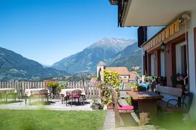 a balcony of a building with tables and chairs and mountains at Garni Dürrenstein in Schenna