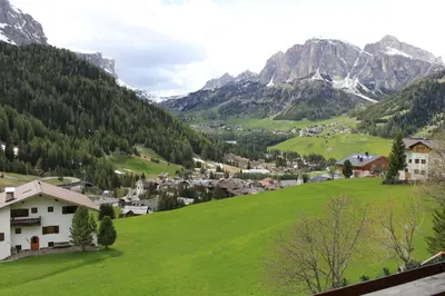a village on a green hill with mountains in the background at Albergo Alisander in Corvara in Badia