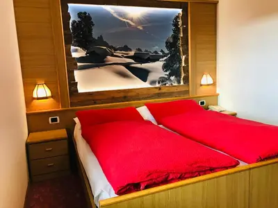 a bed with red pillows and a picture on the wall at Rifugio Capanna Passo Valles in Falcade