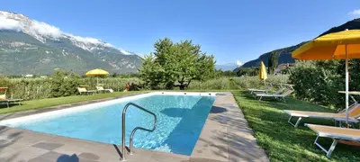 a swimming pool with chairs and an umbrella and mountains at Hotel Greifenstein in Terlano